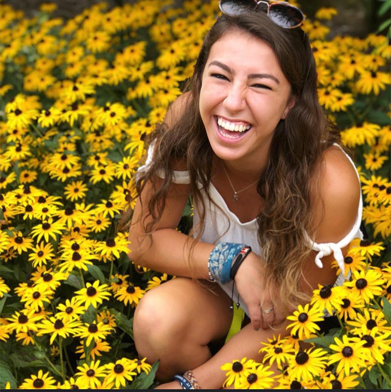 Raquel smiling in a field of flowers.